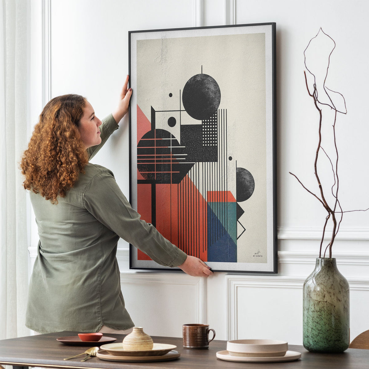geometric abstract wall art in dining room with person adjusting framed canvas on wall with modern decor